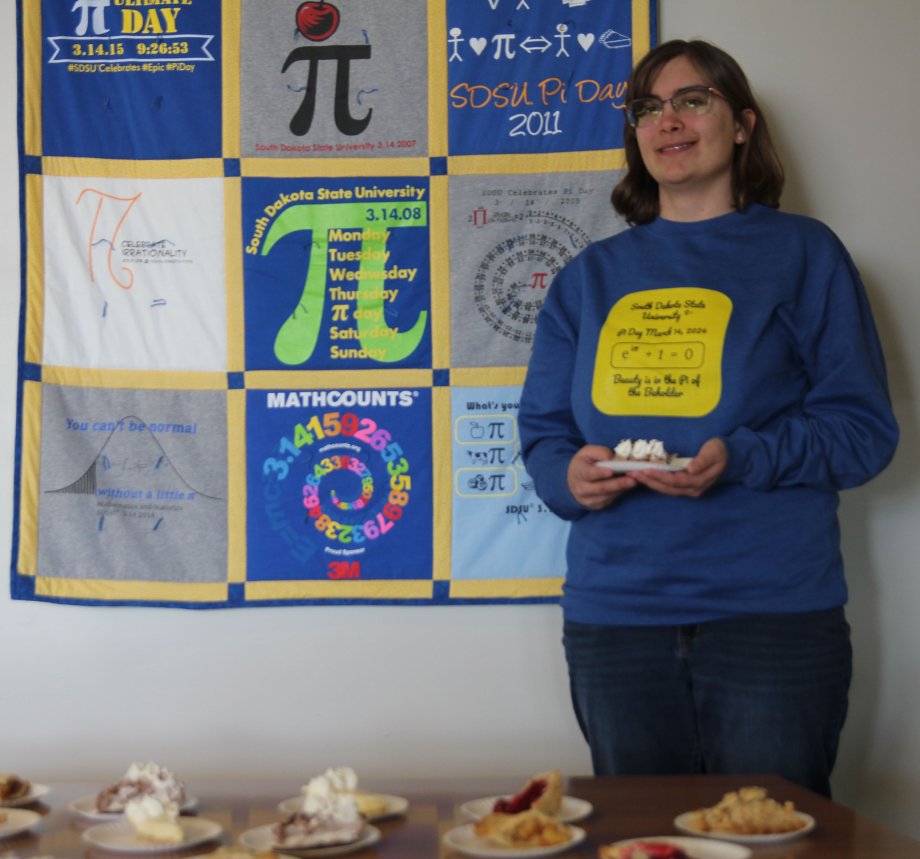 “Beauty is in the Pi of the Beholder" reads the T-shirt of Elizabeth Elsen, a sophomore math and data science major from Yankton. Elsen submitted the winning entry for this year's shirt design. She poses by a quilt made of former Pi Day shirts. Because SDSU was on spring break for actual Pi Day on March 14, the event was observed by the Math Club on March 19.